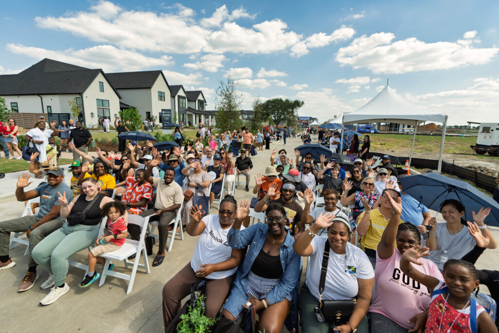 Large diverse group of attendees seated and waving at the Austin Point Open House Party in Fort Bend County.
