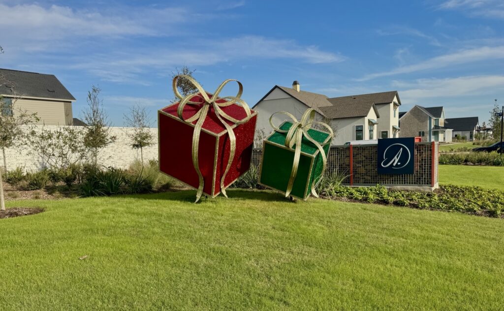 Large holiday gift decorations displayed on the lawn at Austin Point with modern homes in the background