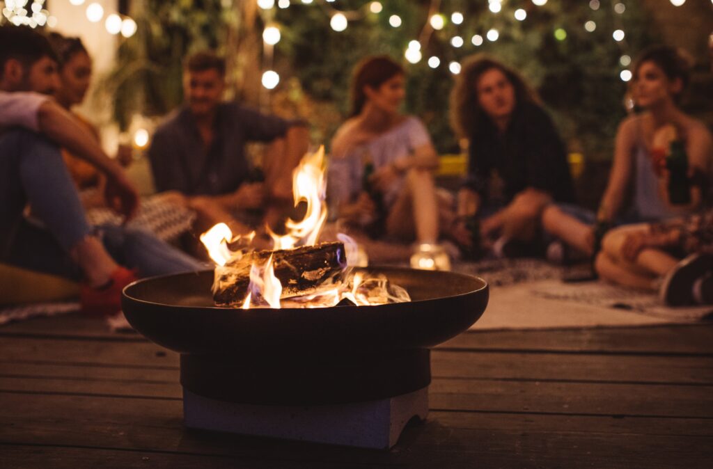 Backyard gathering with friends sitting around a firepit under string lights, creating a cozy and interactive atmosphere
