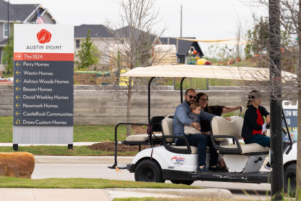 Visitors ride a golf cart past builder signage during the model home tours at Austin Point's Phase One grand opening festival.