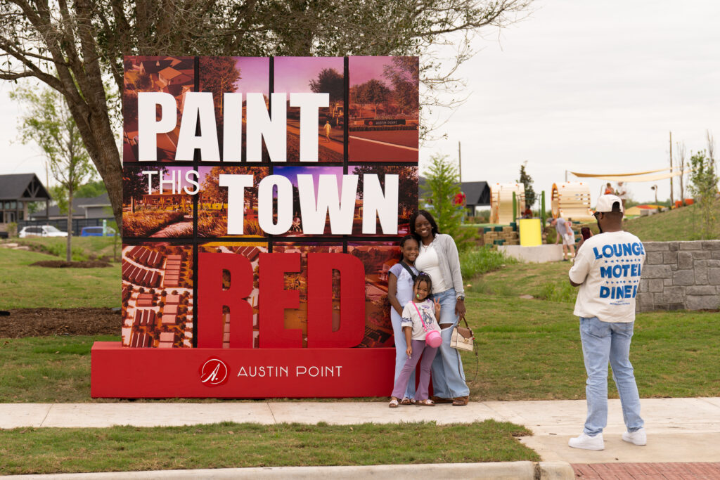 Family posing in front of the Paint This Town Red photo wall during the Austin Point grand opening event.