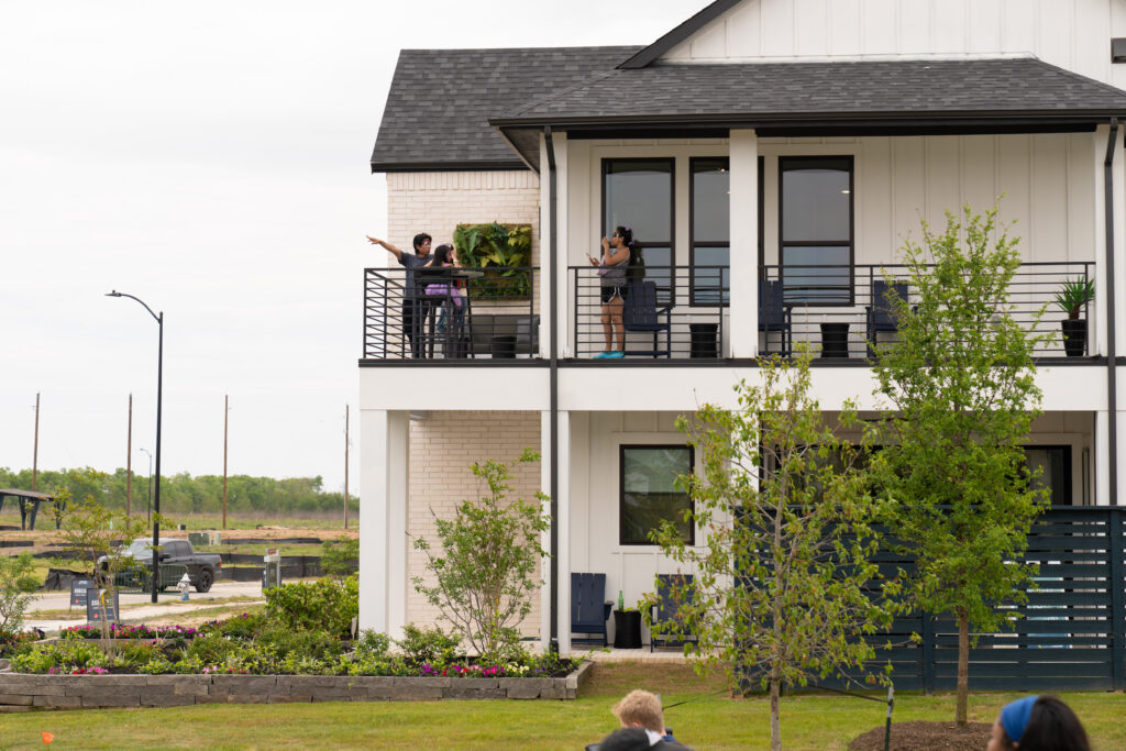 Visitors explore a model home by Drees Custom Homes, stopping on the second story balcony overlooking the neighborhood while enjoying the view and festival activities during Austin Point's Paint This Town Red event at Austin Point.